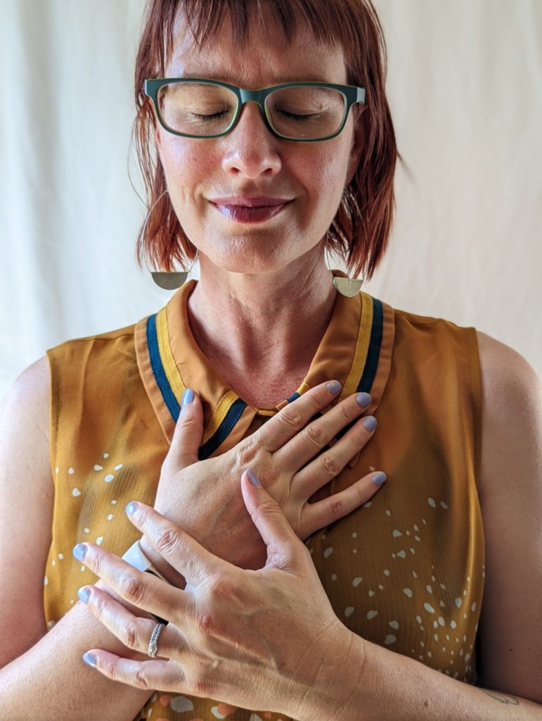 nonbinary person with hands on the heart area of their chest and eyes closed Alana Sanborn narcissistic abuse recovery coach