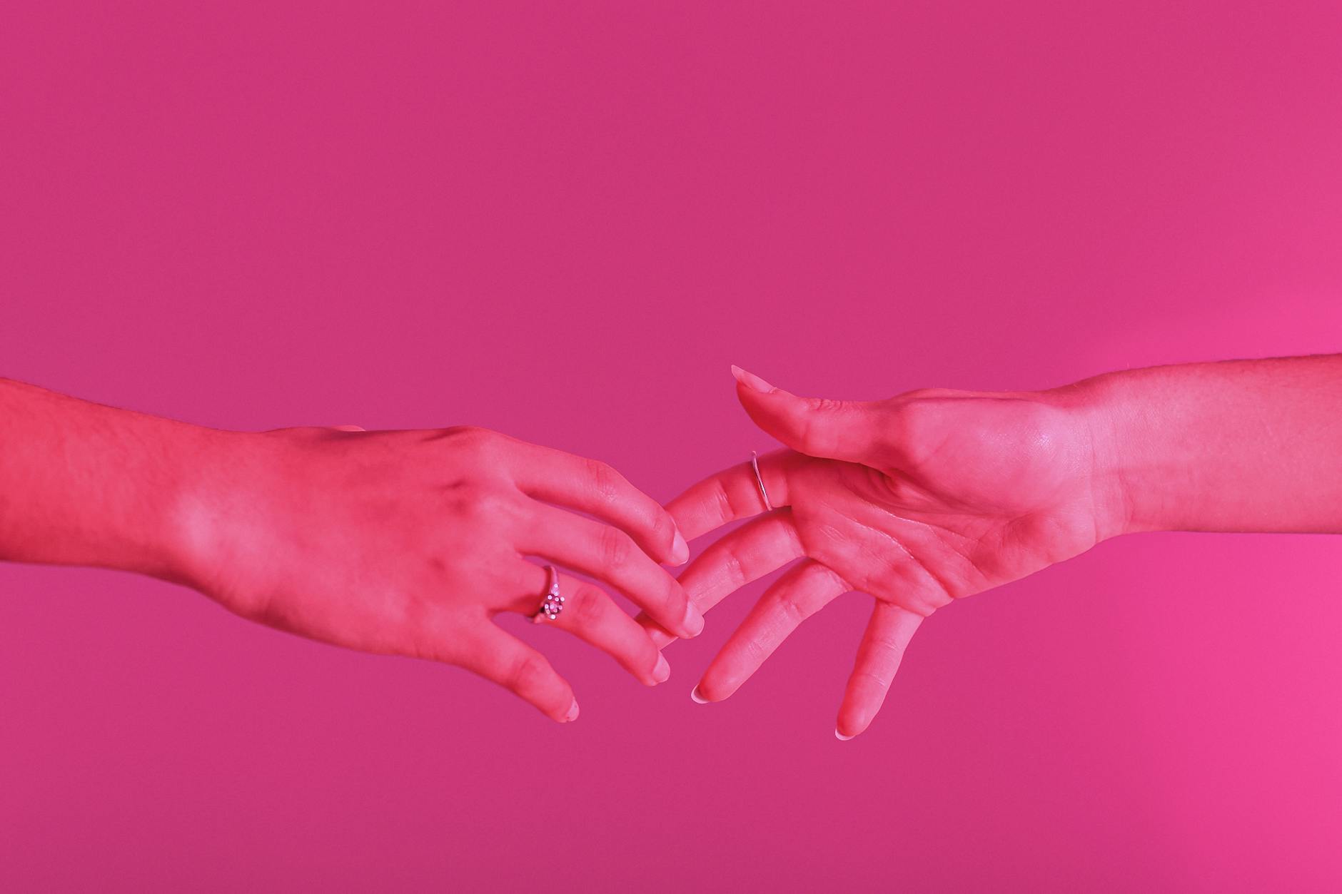 photo of hands touching against pink background